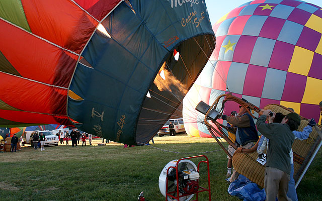 The balloons undergo a "cold inflation" using a gasoline powered fan like the one at the bottom of the picture. Then the propane burners are used to finish the inflation. As the heated air expands and rises it lifts the balloon to a verticle position.